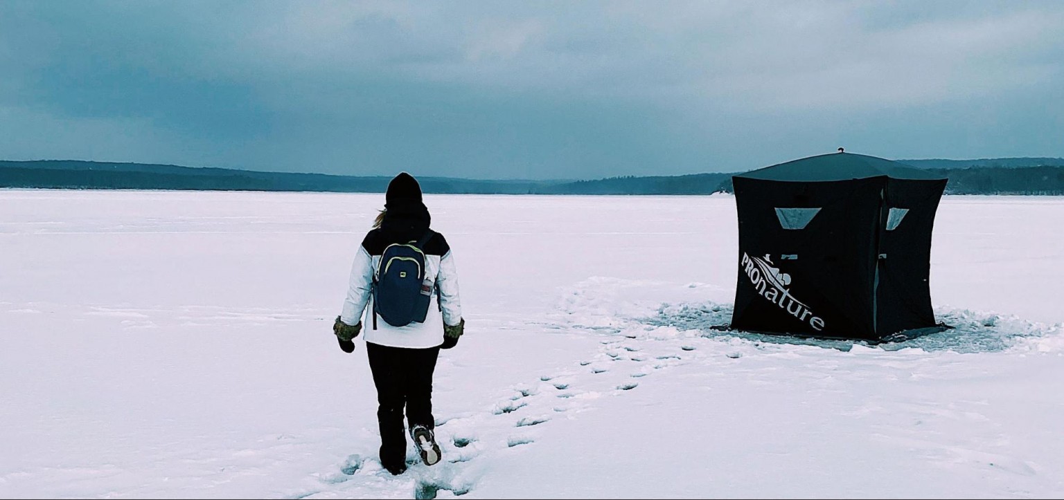 Person walking toward an ice fishing shelter on a frozen lake in the Eastern Townships of Quebec.