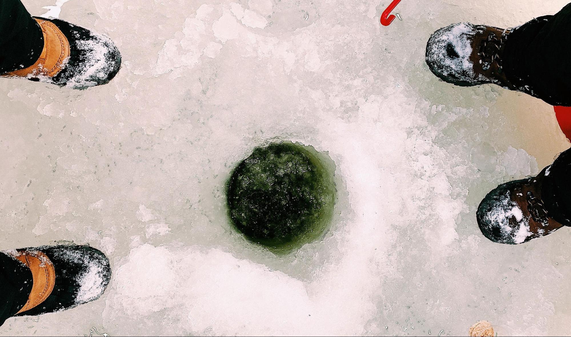 Ice fishing hole on a frozen lake in the Eastern Townships of Quebec, surrounded by winter boots and snow.