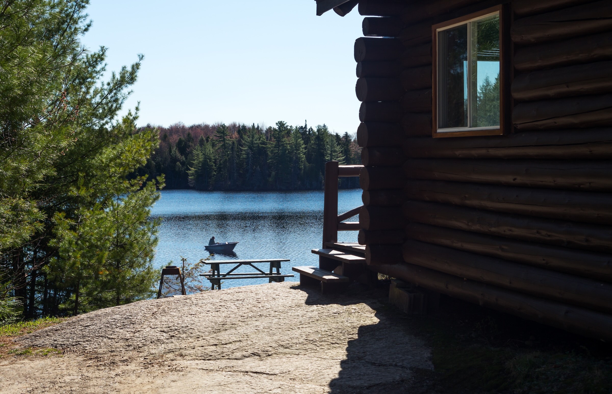 Rustic fishing cottage beside a Quebec lake with a small boat on the water surrounded by forest.