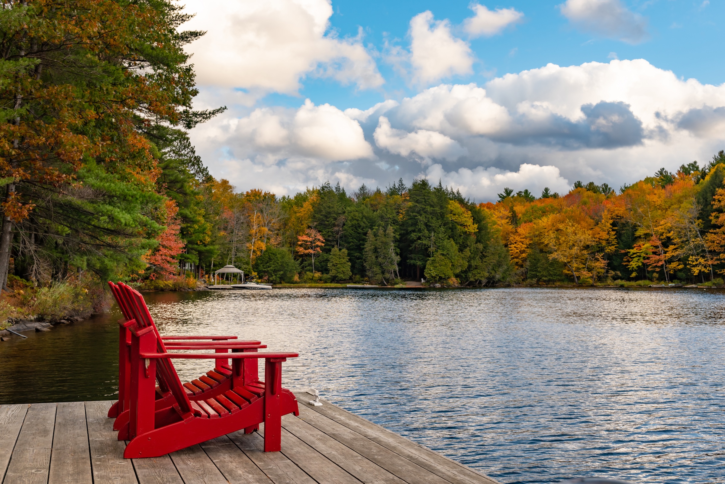 Red Adirondack chairs on a lakefront dock in Quebec surrounded by colorful fall foliage, ideal for a fishing cottage getaway.