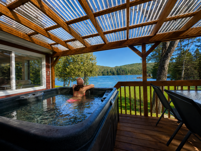 Femme relaxant dans le spa en admirant le lac du Chalet à louer Le Cardinal à Lanaudière, chalet avec spa à Chertsey.