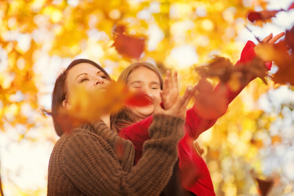 Parent and child playing with colourful fall leaves in Quebec