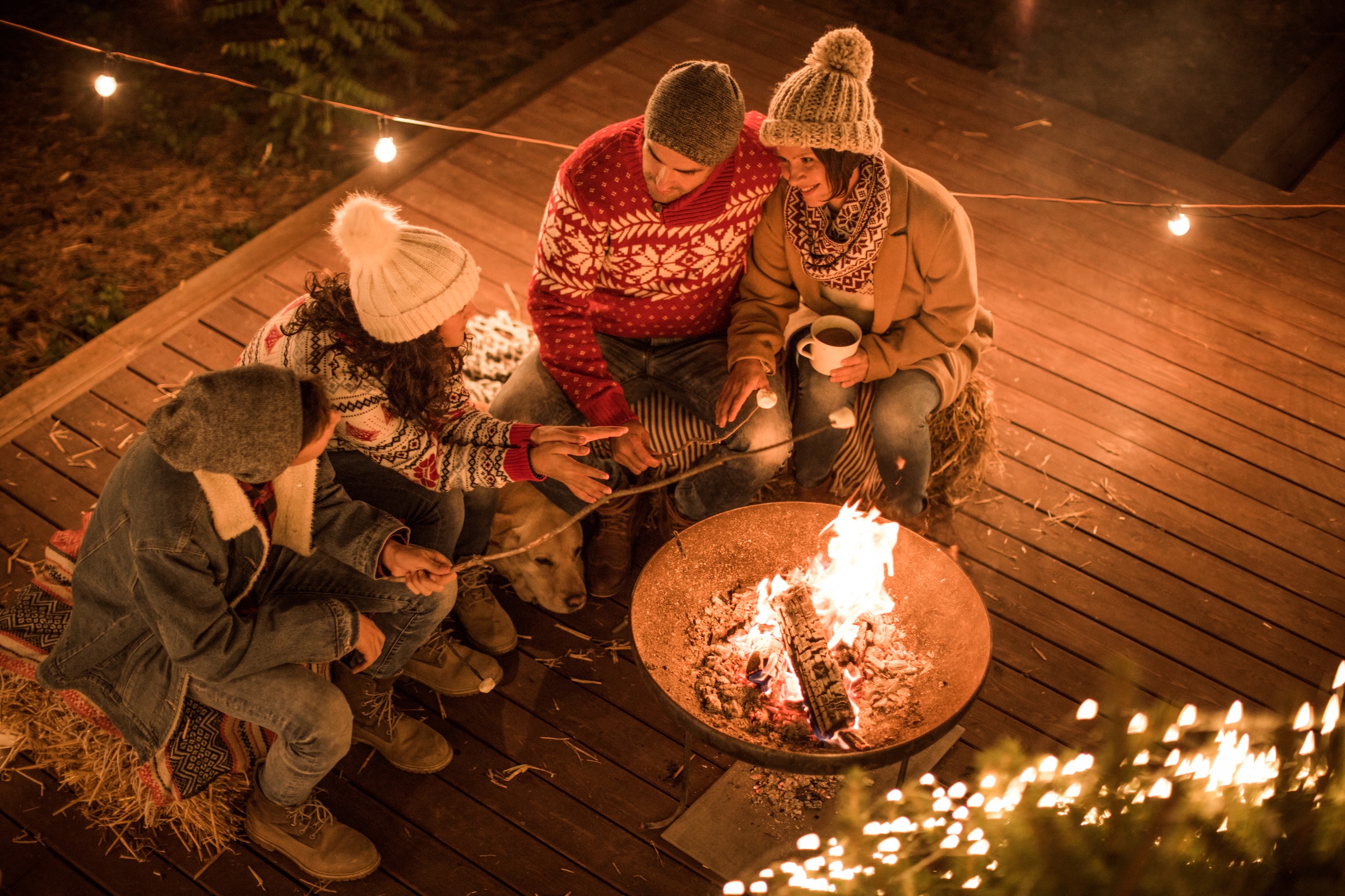 Family gathered around an outdoor fire on the deck of a cottage in Quebec.